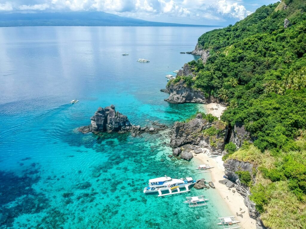 Apo Island-kustlijn met helderblauw water en boten langs een tropisch strand in de Filipijnen.
