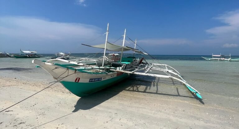 Traditionele Filipijnse bangka boot aan het strand van Siargao met helder water, wit zand en blauwe lucht op de achtergrond.
