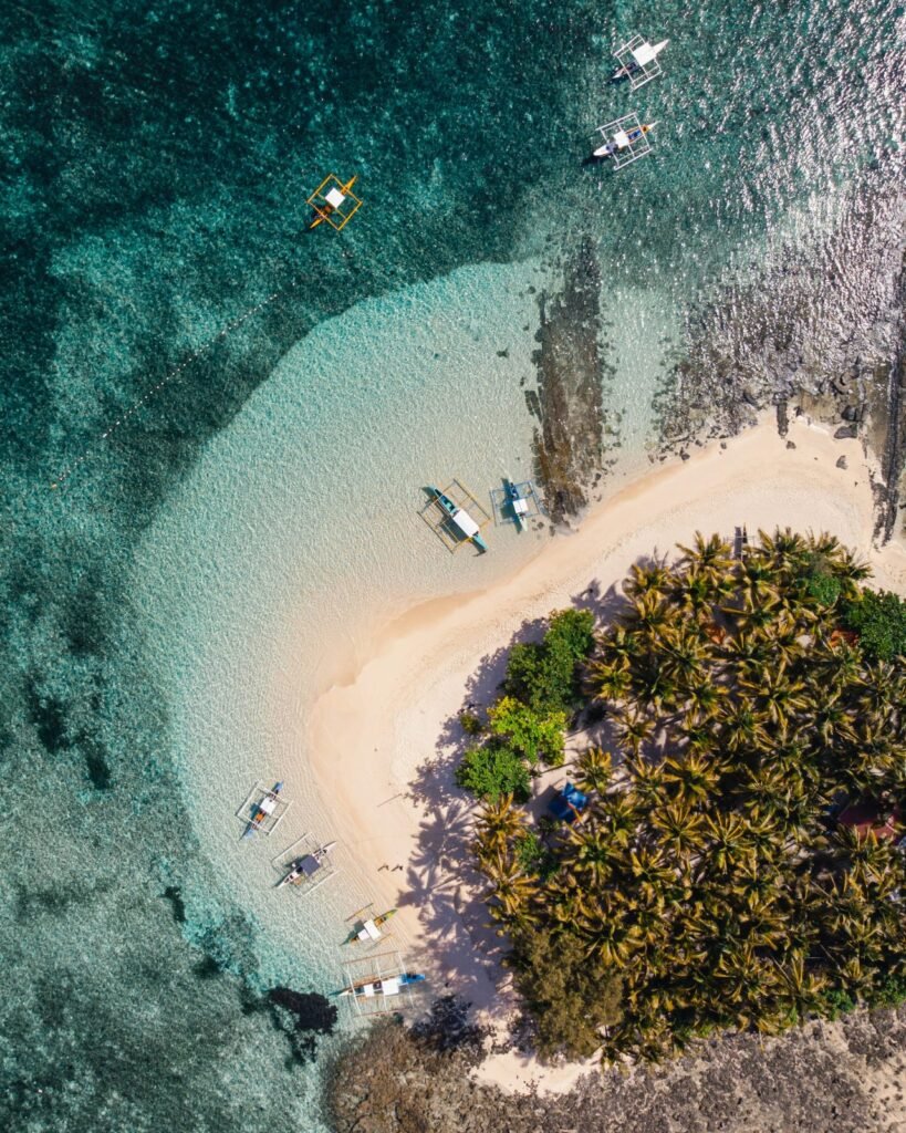 Dronefoto van een tropisch strand bij Siargao met palmbomen, wit zand, turquoise water en traditionele boten.