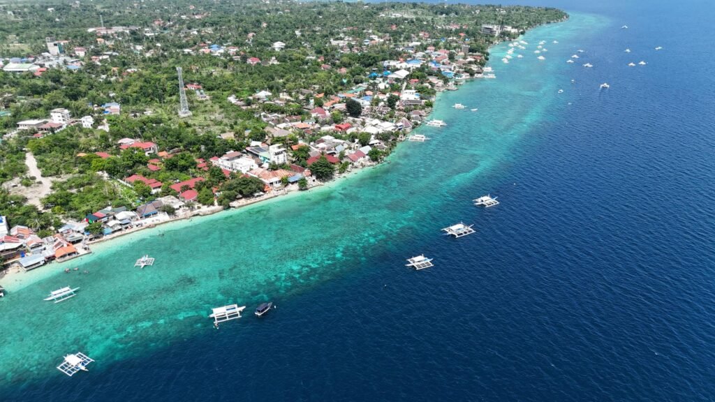 Luchtfoto van een kustdorp in Cebu met turquoise water, traditionele Filipijnse boten en tropische begroeiing langs de kustlijn.